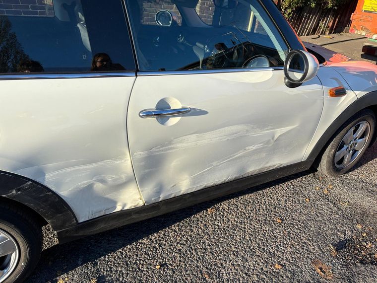 White MINI Cooper with the driver's door and rear quarter dented down the side