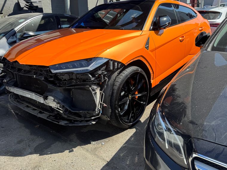 Orange Lamborghini Urus with the front bumper and headlight torn out after a collision